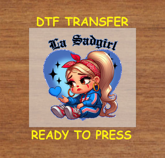 “La Sadgirl” ready to press DTF transfer! This cute design features the text "La Sadgirl" with sad Chicano character with a blue heart accent.