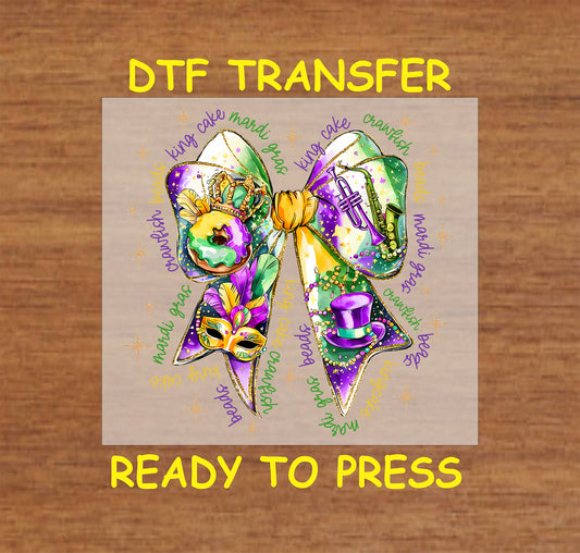 DTF transfer featuring a colorful Mardi Gras bow with beads, king cake, a mask, a trumpet, and a top hat in festive purple, green, and gold.