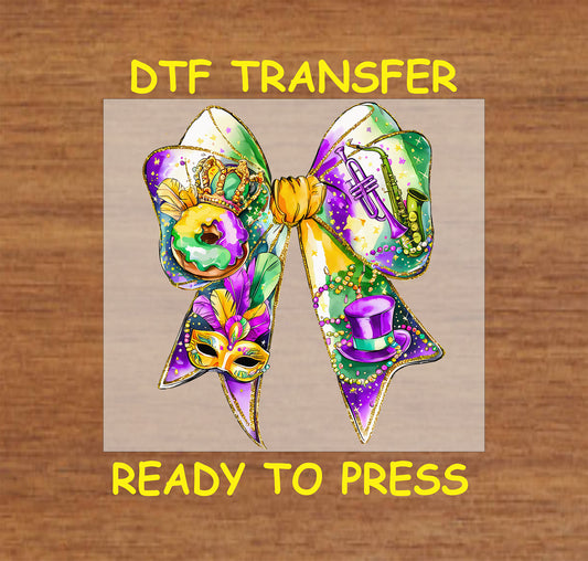 DTF transfer featuring a vibrant Mardi Gras bow with king cake, a mask, a trumpet, beads, and a top hat in festive purple, green, and gold.