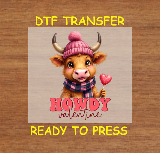 "Howdy Valentine" DTF Transfer featuring an adorable highland cow wearing a pink hat and scarf, holding a heart-shaped lollipop, perfect for Valentine-themed shirts and crafts.