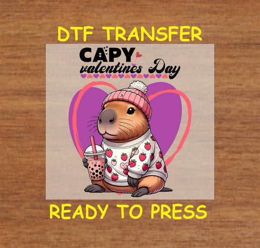 "DTF transfer with a capybara wearing a strawberry sweater and pink beanie, holding boba, on a pink and purple Valentine's Day background."