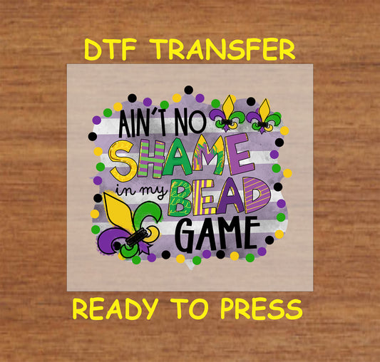 Mardi Gras DTF transfer with "Ain't No Shame in My Bead Game" text, beads, and fleur-de-lis.