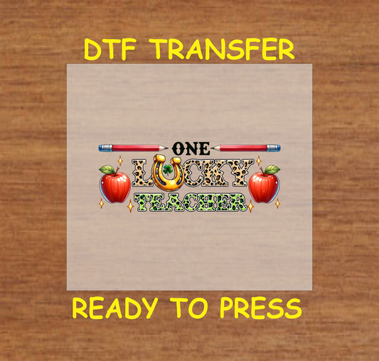 St. Patrick’s Day DTF transfer featuring "One Lucky Teacher" text with apples, pencils, and a horseshoe.