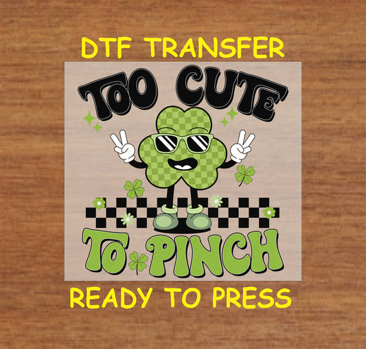 St. Patrick’s Day kids DTF transfer with "Too Cute to Pinch" text, a shamrock character, sunglasses, and checkered background.