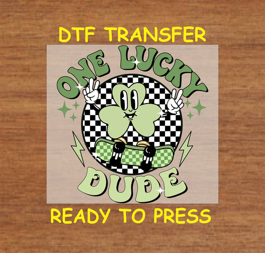 St. Patrick’s Day kids DTF transfer with "One Lucky Dude" text, skateboarding shamrock character, checkered background, and lightning bolts.