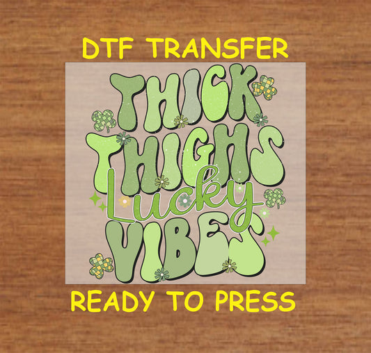 St. Patrick’s Day DTF transfer with bold green text reading “Thick Thighs Lucky Vibes,” decorated with shamrocks and sparkles.