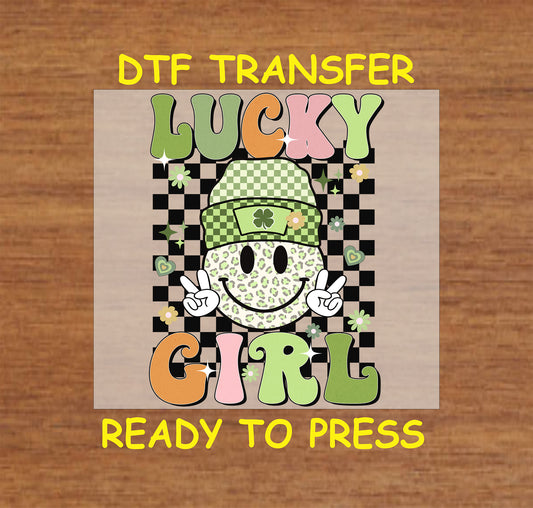 St. Patrick’s Day DTF transfer featuring a leopard-print smiley face in a shamrock beanie with “Lucky Girl” text and a checkered background.