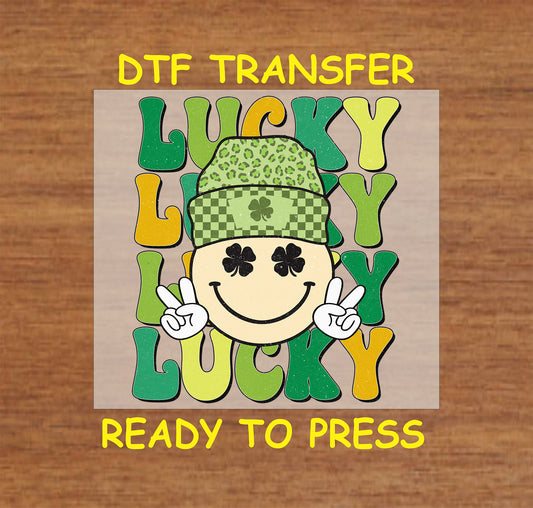 St. Patrick’s Day DTF transfer featuring a smiley face with shamrock eyes, a green checkered beanie, and bold “LUCKY” text in vibrant colors.