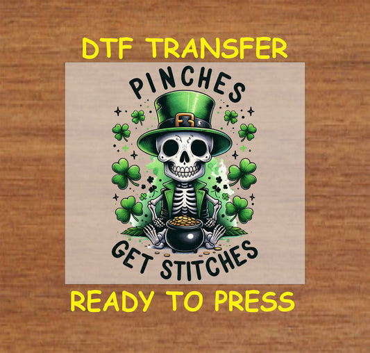 Skeleton leprechaun with a pot of gold and shamrocks, featuring "Pinches Get Stitches" text.