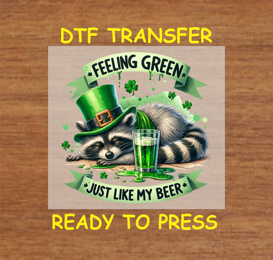 Sleepy raccoon in a leprechaun hat with green beer and “Feeling Green Just Like My Beer” text.