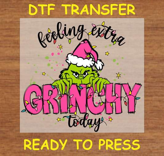 Green Grump-themed DTF transfer featuring a green character in a Santa hat, with pink text saying "Feeling Extra Today" and colorful Christmas lights.